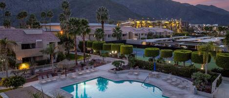 A resort with a swimming pool, lounge chairs, and a mountainous backdrop.