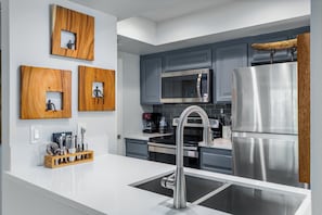 A modern kitchen with stainless steel appliances, wooden wall decor, and a white countertop. - Casa del Segundo | MCM 1BR | 2 Pools & Tennis | Palm Springs (Palm Springs)