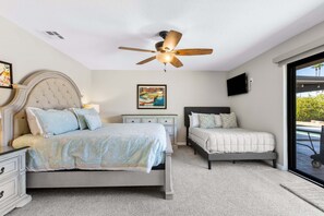 A bedroom with two beds, a ceiling fan, a painting, a TV, and a view of the outdoors. - Boqueron and Beyond | Private Pool & Spa | Entertainer's Backyard | 3BR | Bermuda Dunes (Bermuda Dunes)
