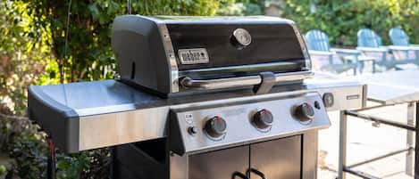 Una parrilla de gas Weber GS4 con acabado de acero inoxidable, un termómetro digital y un quemador lateral.