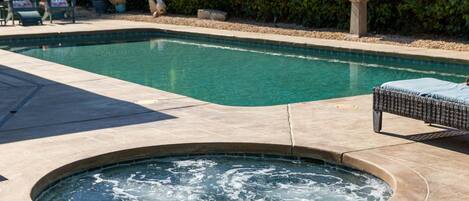Una piscina con hidromasaje, rodeada por un patio con sillas y una fuente.