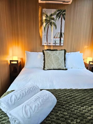 Een hotelkamer met een groot bed, twee bedlampen, een schilderij van palmbomen en een groen, gertextureerd plaid.