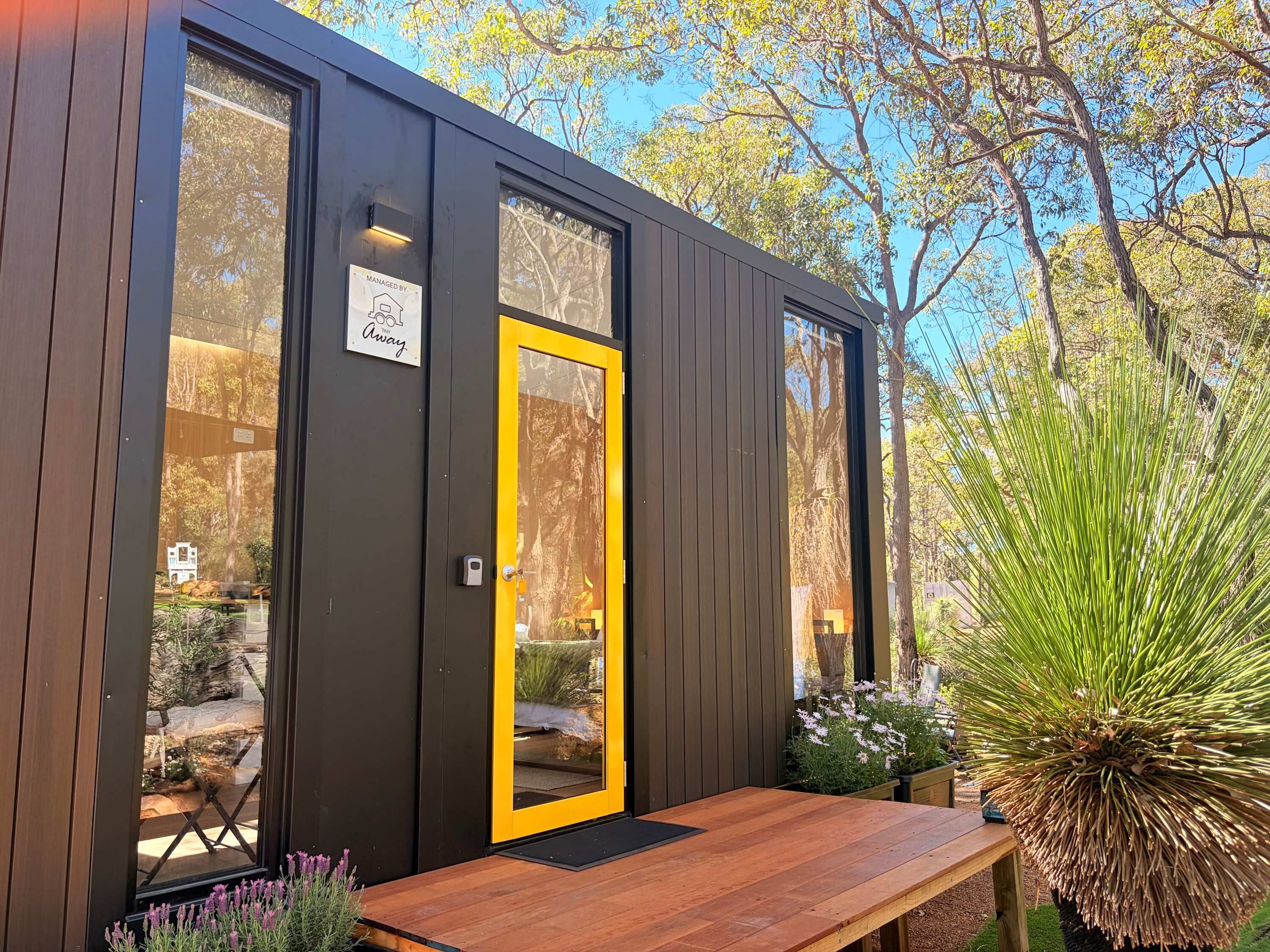 A modern wooden building with a yellow door, large windows, and a wooden bench outside.