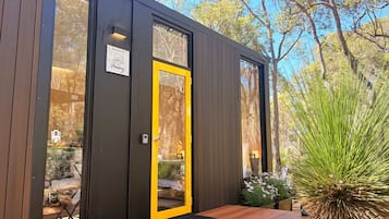 A modern wooden building with a yellow door, large windows, and a wooden bench outside.