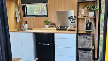 Een kleine keuken met een magnetron, spoelbak en opslagkasten.