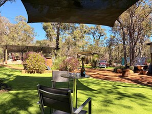 A patio area with a table and chairs, surrounded by lush greenery and a vintage car.