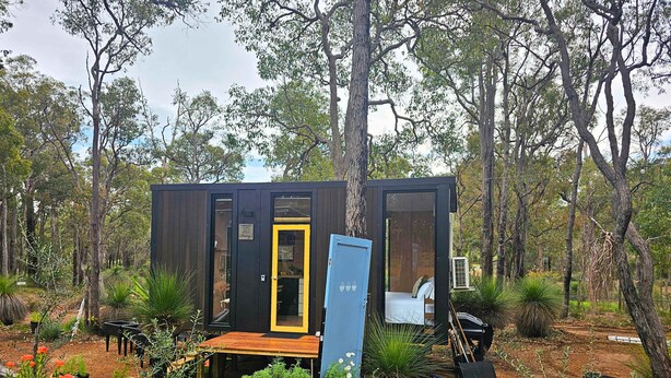 Una cabana petita i moderna amb terrassa, envoltada d'un jardí i arbres.
