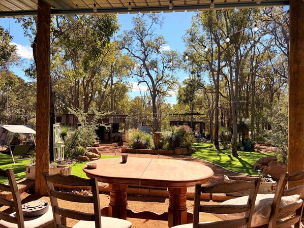 An outdoor dining area with a round table and chairs, surrounded by trees and a well-maintained lawn.