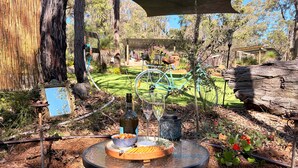 An outdoor dining area with a round table, a bottle, a glass, and a bowl of snacks.