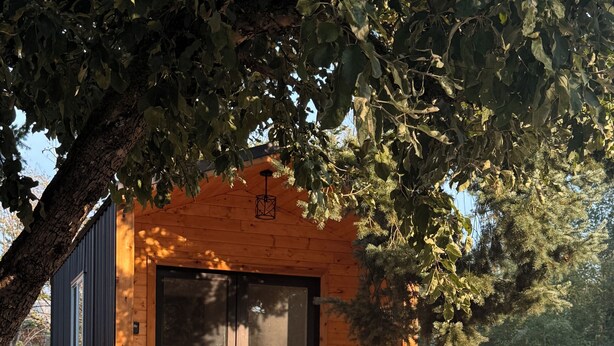 A wooden cabin with a large window and a door, a hammock, and a red chair.