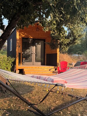 A wooden cabin with a large window and a door, a hammock, and a red chair.