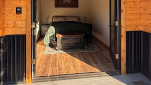 A wooden interior with a bed, a 'Relax' sign, and a door leading to an outdoor area.