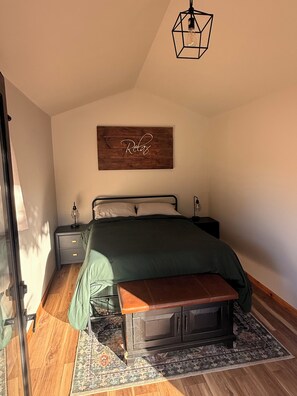 Un dormitorio con cama, mesitas de noche, un banco, un tapete y un letrero de madera en la pared.