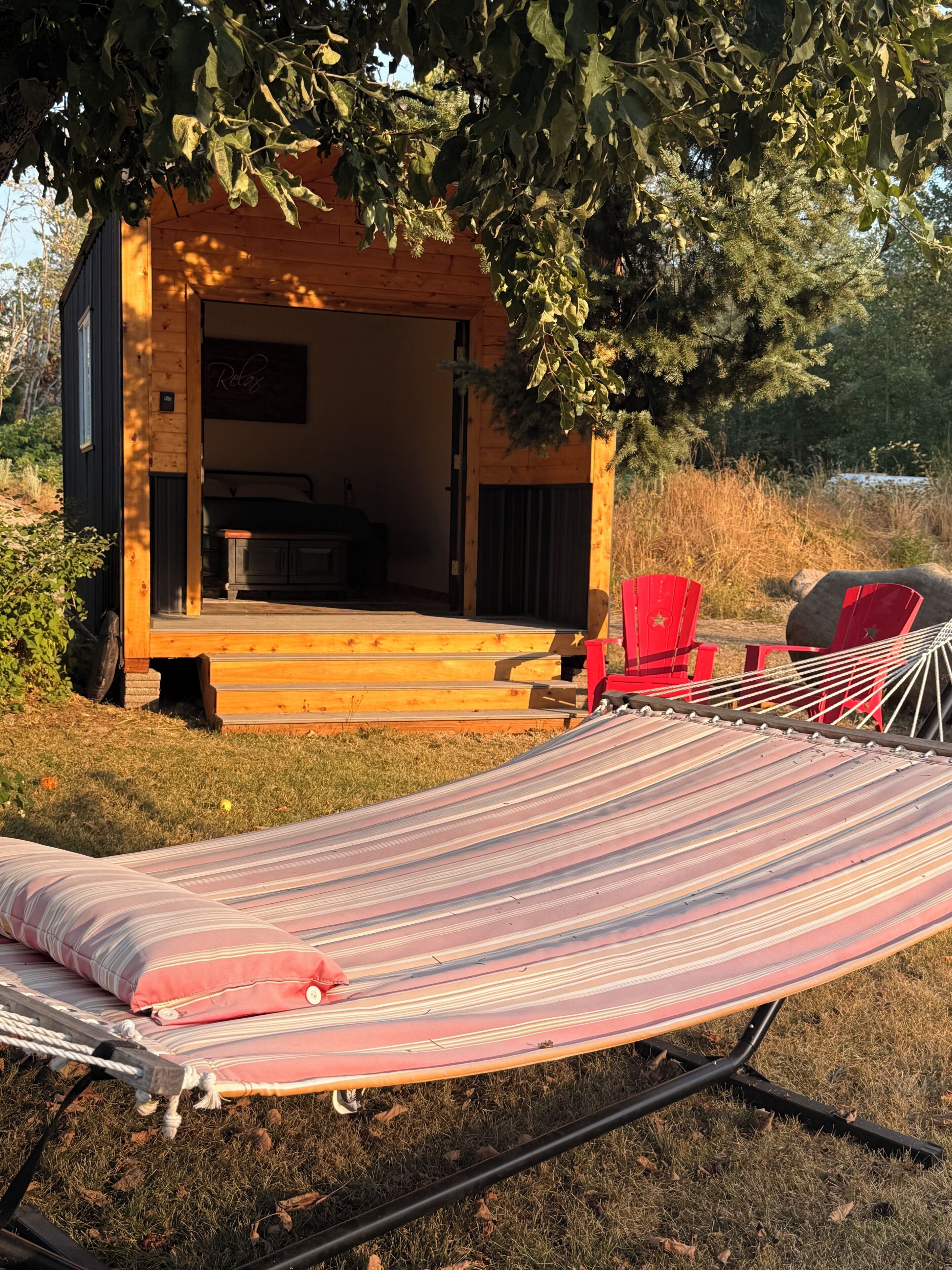 Une cabane en bois avec un hamac et des chaises rouges à l’extérieur.