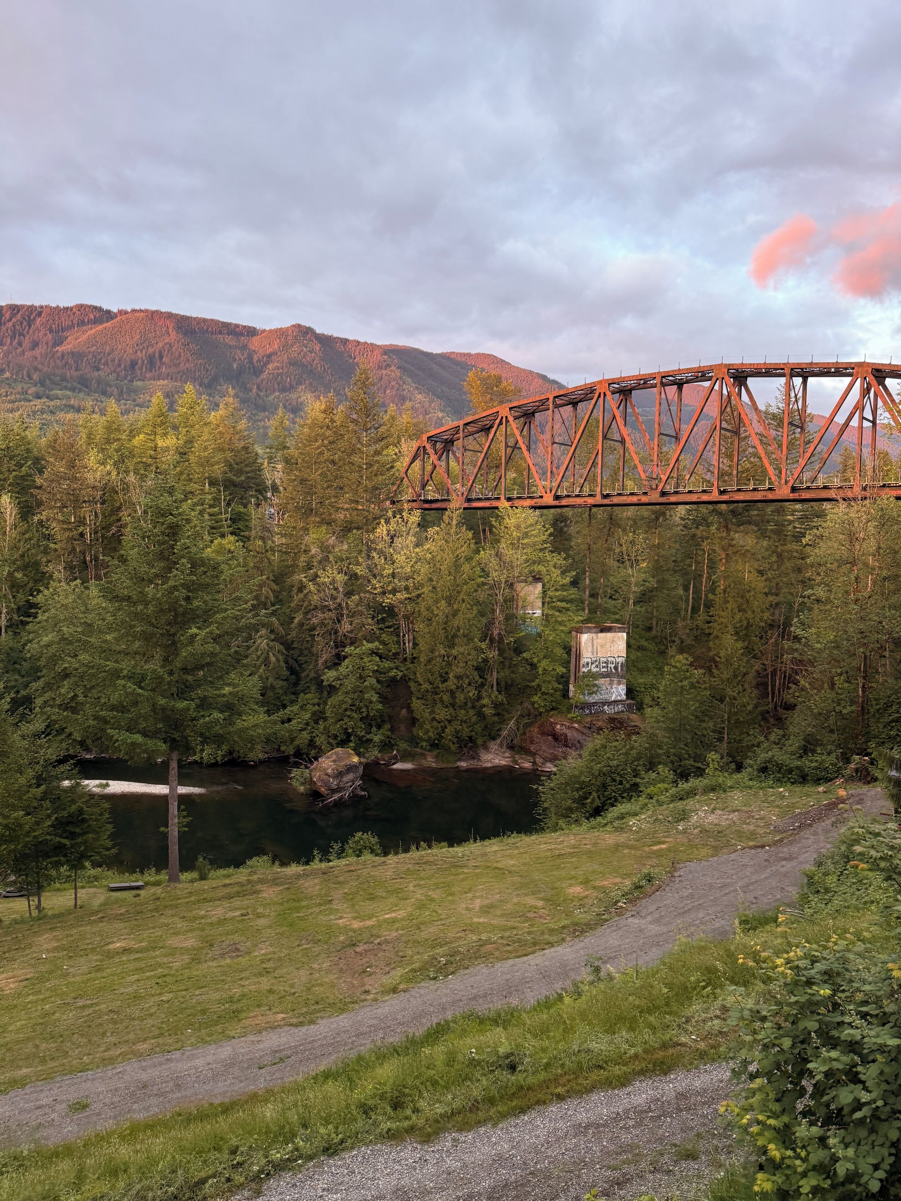 A bridge over a river with a forested area and mountains in the background.