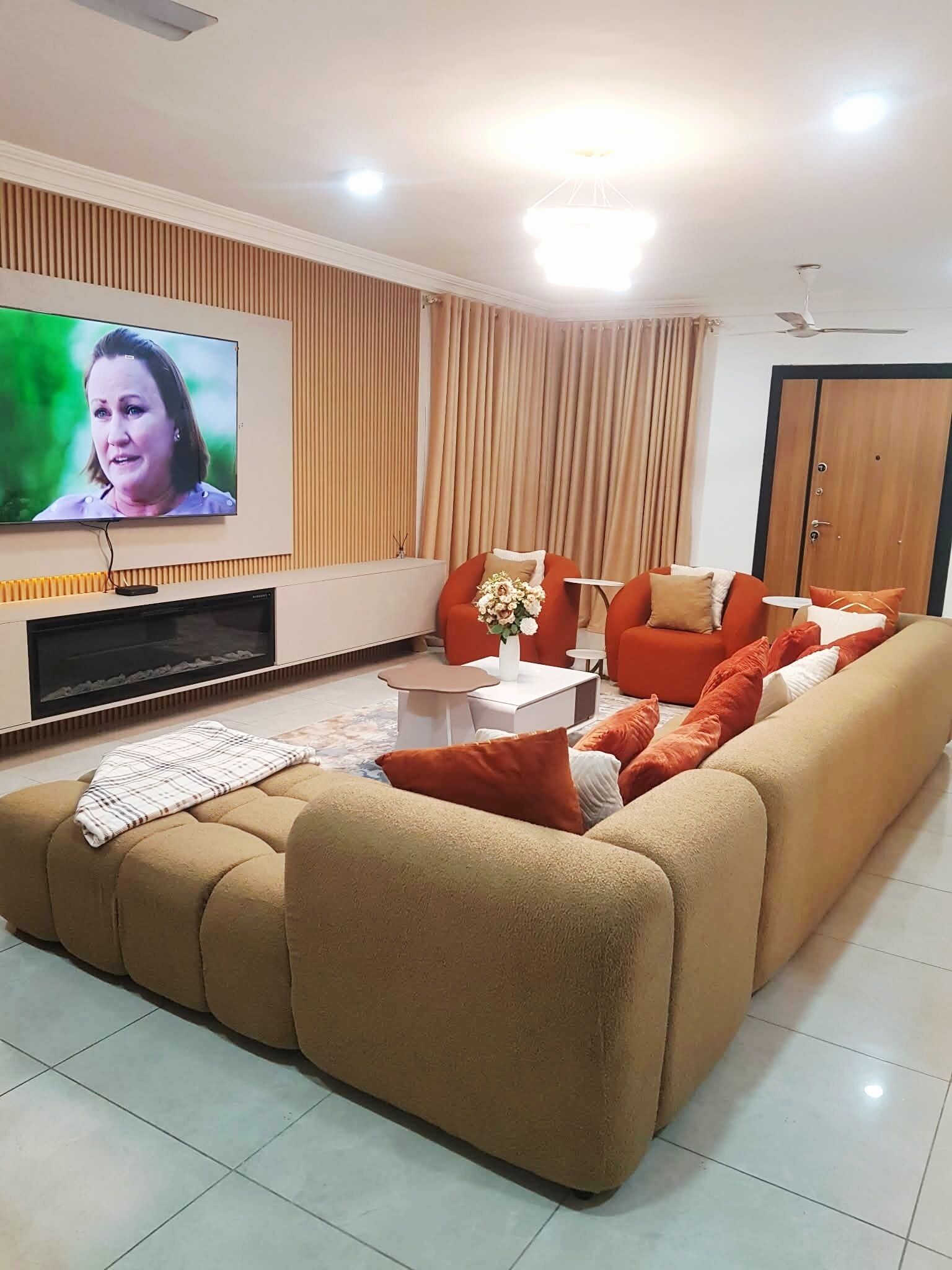 A living room with a large flat-screen TV, a sofa, a coffee table, and a fireplace.
