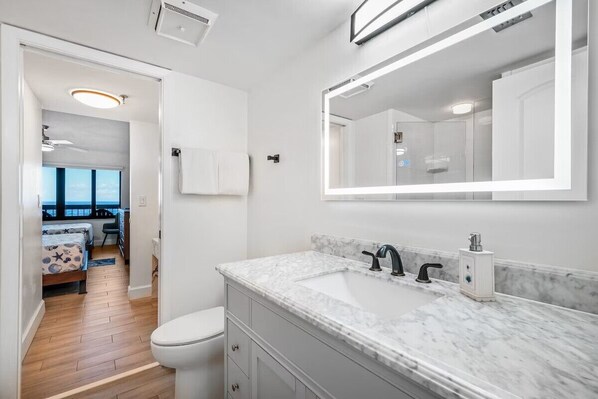 A modern bathroom with a marble countertop, a large mirror, and a toilet. - Beautiful, Direct Oceanfront 3/3 Ocean Front Condo (Ormond Beach)