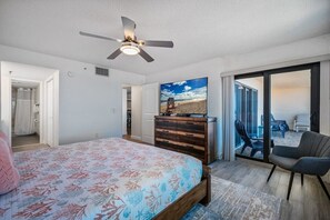 Ein Schlafzimmer mit Bett, Deckenventilator, Kommode und Blick auf den Strand durch eine Schiebetür.