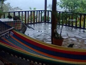 A hammock on a stone-tiled floor with a railing and potted plants.