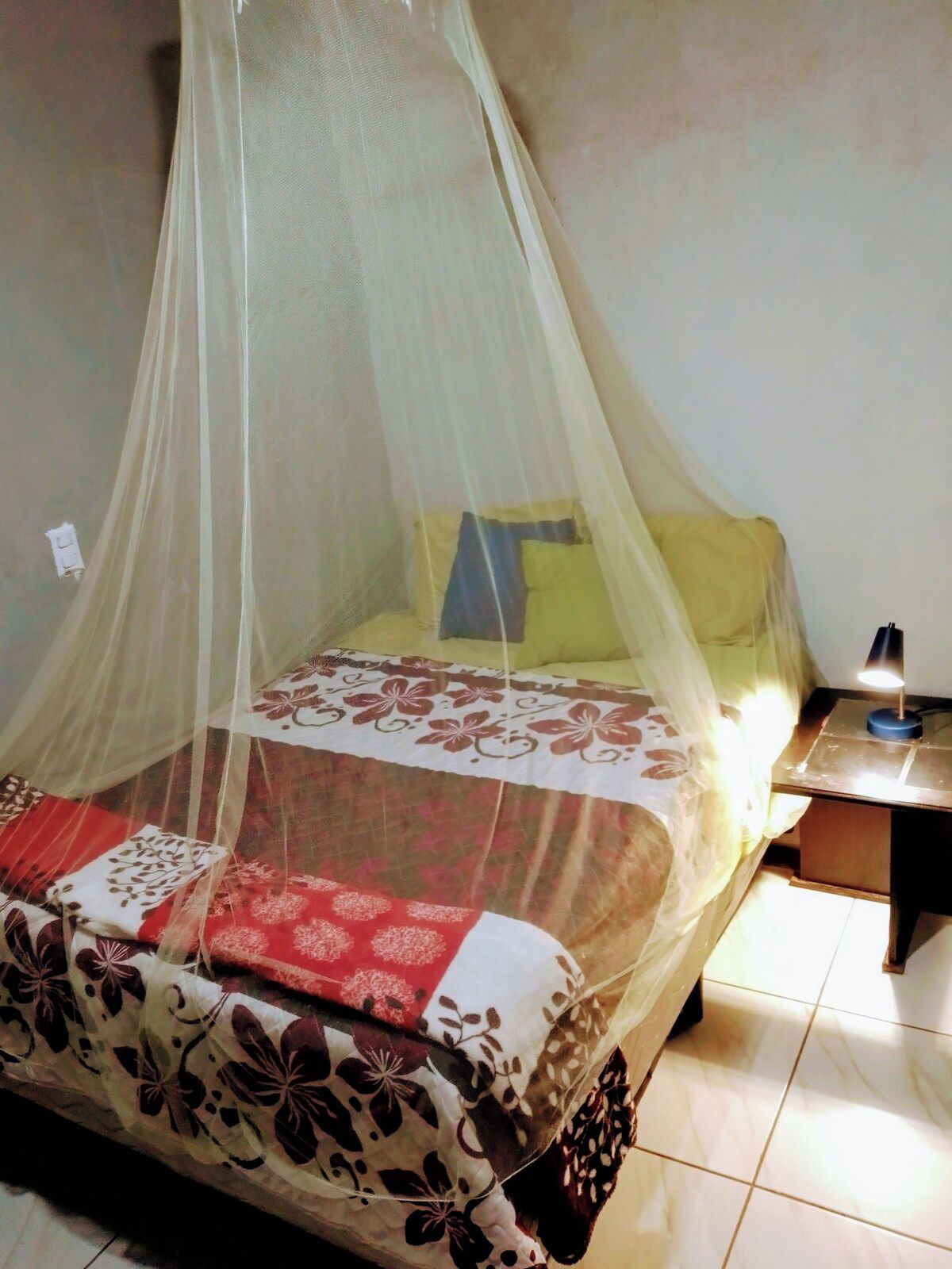 Un lit à baldaquin, une table de chevet avec une lampe et une couvre-lit à motifs.