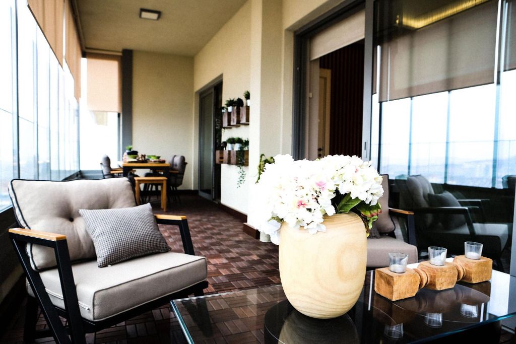 A modern lounge area with a sofa, a table with a vase of flowers, and a view through large windows.