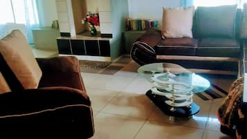 Una sala de estar con sofá, sillón y una mesa de centro. Hay una chimenea con repisa y estanterías.