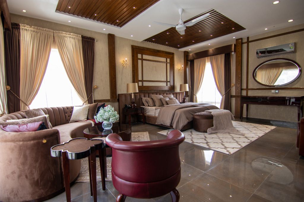 A hotel room with a sofa, a red armchair, a bed with a headboard, a mirror, and a ceiling fan.