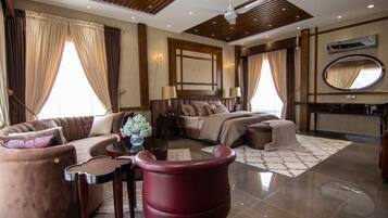 A hotel room with a sofa, a red armchair, a bed with a headboard, a mirror, and a ceiling fan.