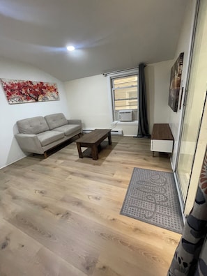 Een woonkamer met een bank, een salontafel, een raam met gordijnen en een radiator.