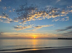 Un coucher de soleil sur une étendue d’eau calme, avec une côte visible au loin.