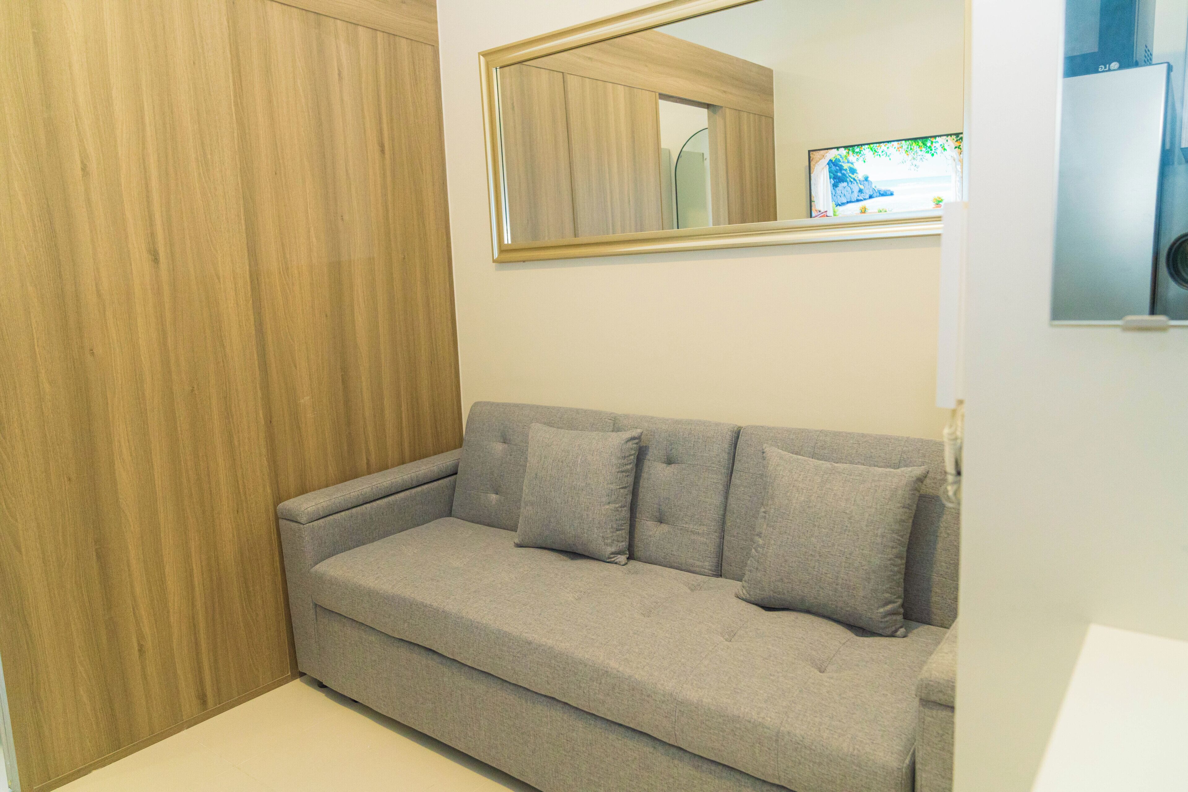 Une pièce avec un canapé gris, une armoire en bois et un miroir au mur.