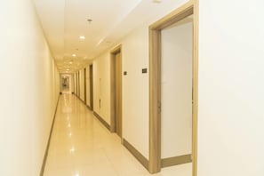 Un couloir d’hôtel avec des portes des deux côtés, un sol carrelé et des luminaires encastrés au plafond.