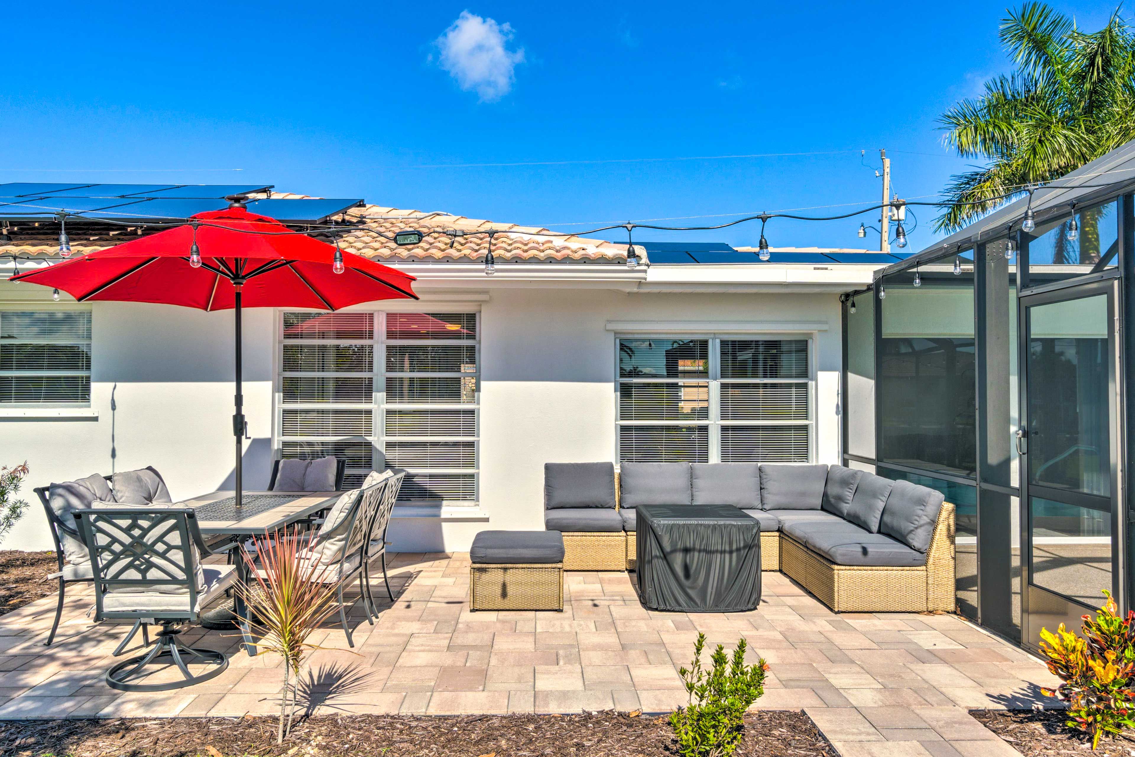 A patio with outdoor furniture, a red umbrella, and a glass-enclosed room.