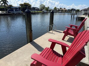 Ein Steg am Wasser mit roten Adirondack-Stühlen und einem Boot.
