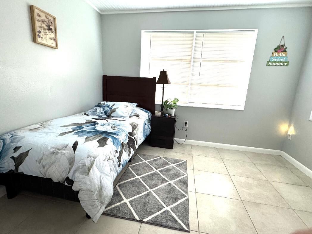 Un dormitorio con cama, mesita de noche, lámpara, ventana con persianas y un adorno en la pared.