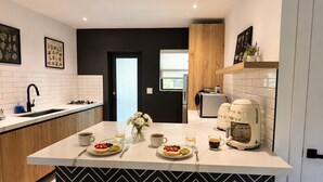 Cozinha moderna com ilha central, azulejos brancos, painel de mosaico em chevron preto e branco e máquina de café.