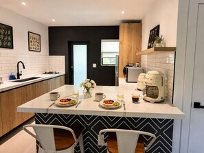 A modern kitchen with a central island, white tiles, a black and white chevron backsplash, and a coffee machine. - Comfortable Interior • Cozy Retreat • Outdoor Living (Miami)