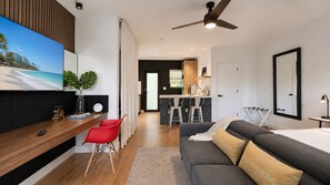 A modern hotel room with a bed, a desk, a red chair, a sofa, a ceiling fan, and a kitchen area in the background. - Comfortable Interior • Cozy Retreat • Outdoor Living (Miami)