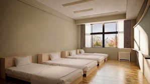 Une pièce avec quatre lits alignés contre un mur, une grande fenêtre avec des rideaux et un radiateur posé sur le sol.