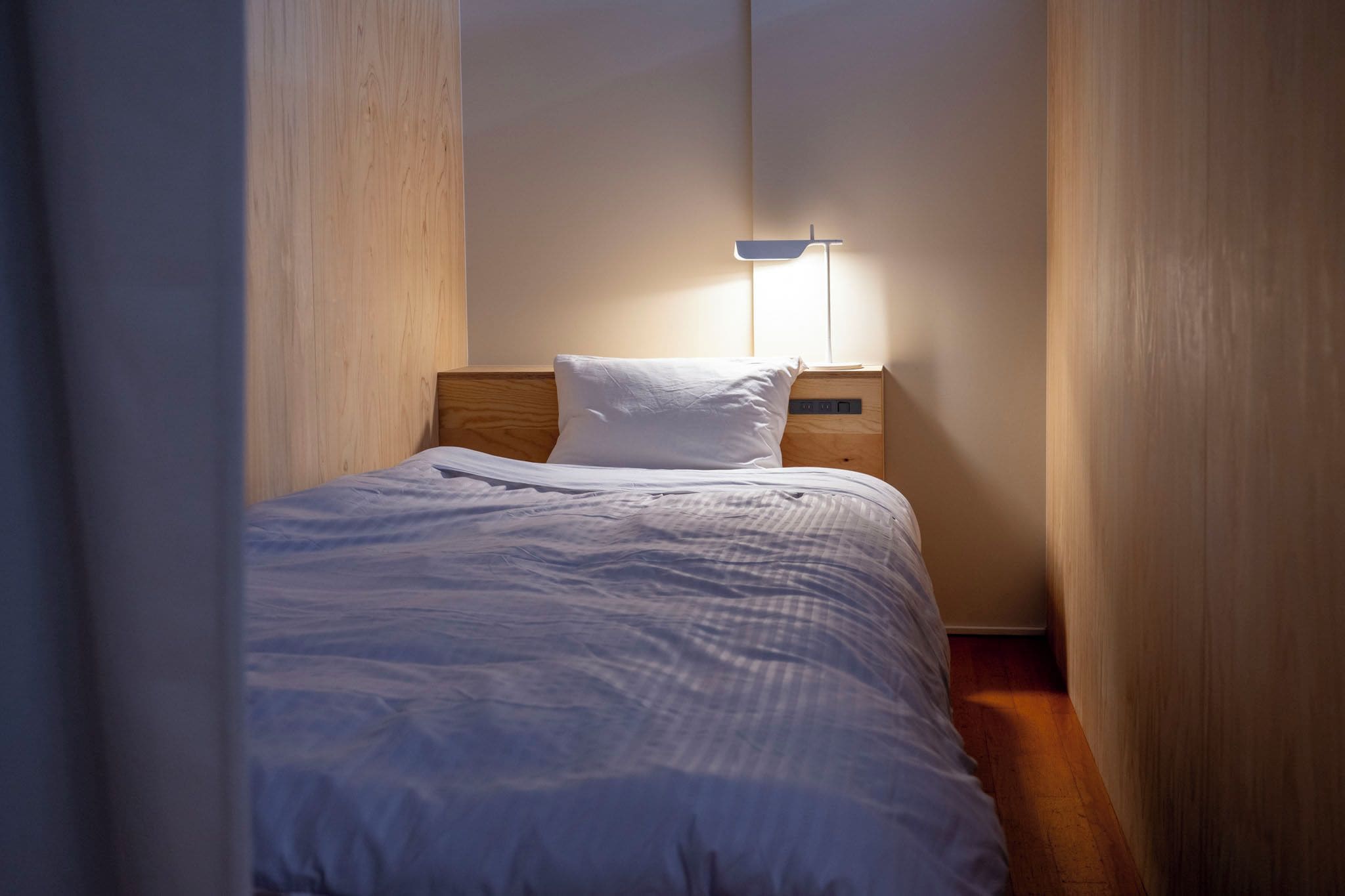 Una stanza piccola con un letto, un comodino e una lampada a muro.