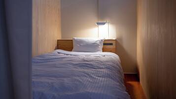 A narrow room with a bed, a nightstand, and a wall-mounted lamp.