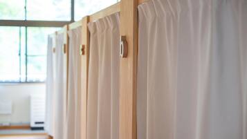 A row of wooden dividers with a light-colored curtain in a room with large windows.