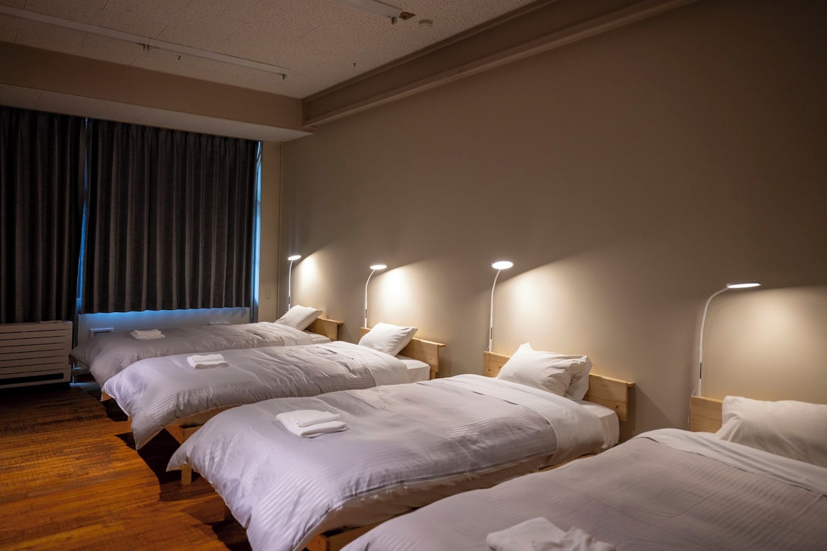 A hotel room with four single beds, each with a bedside table and lamp.