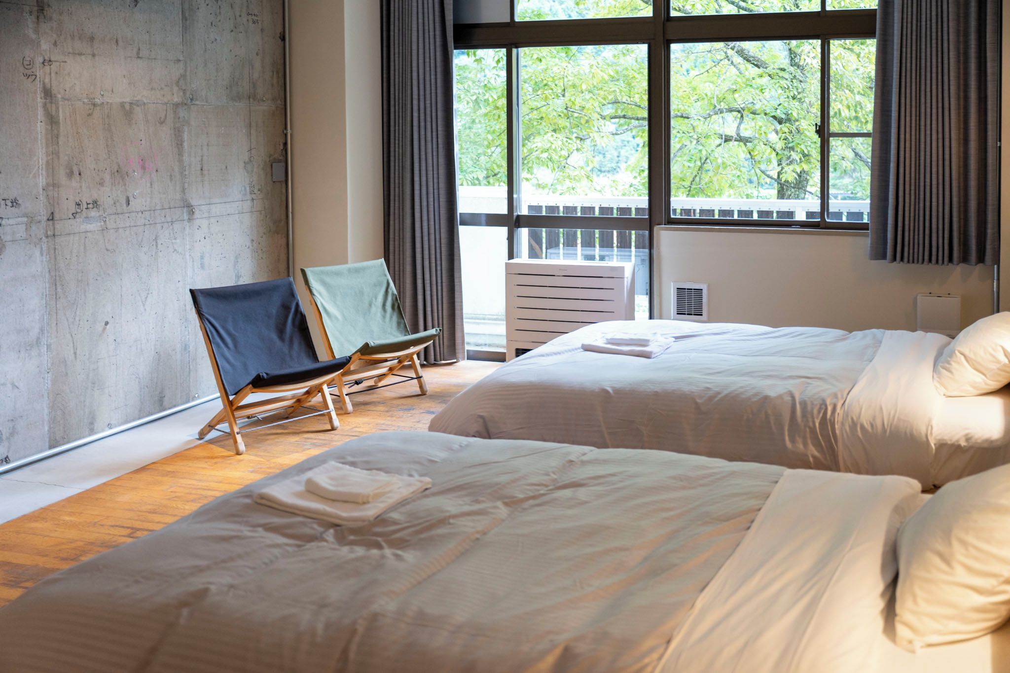 A hotel room with two beds, a large window, and a chair.