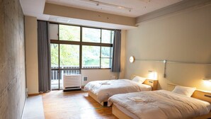 A hotel room with two beds, a large window with curtains, a radiator, and a bedside table with a lamp.