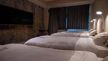 A hotel room with two beds, a flat-screen TV mounted on the wall, a desk with a chair, and a window with curtains.