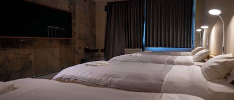A hotel room with two beds, a flat-screen TV mounted on the wall, a desk with a chair, and a window with curtains.