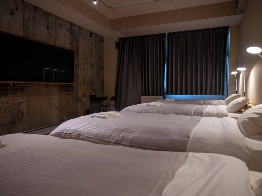 A hotel room with two beds, a flat-screen TV mounted on the wall, a desk with a chair, and a window with curtains.