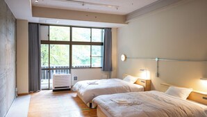 A hotel room with two beds, a large window with curtains, a ceiling light, and a wall-mounted heater.