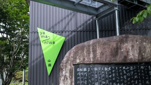 A building with a green triangular sign and a stone structure with Japanese characters.